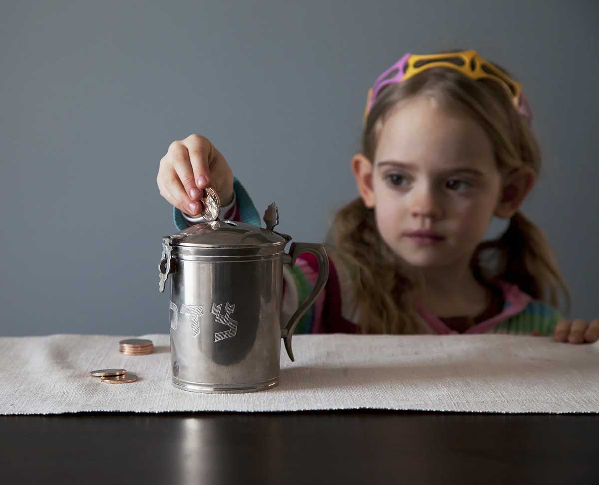 Girl Drops Coins Into Tzedakah Jar